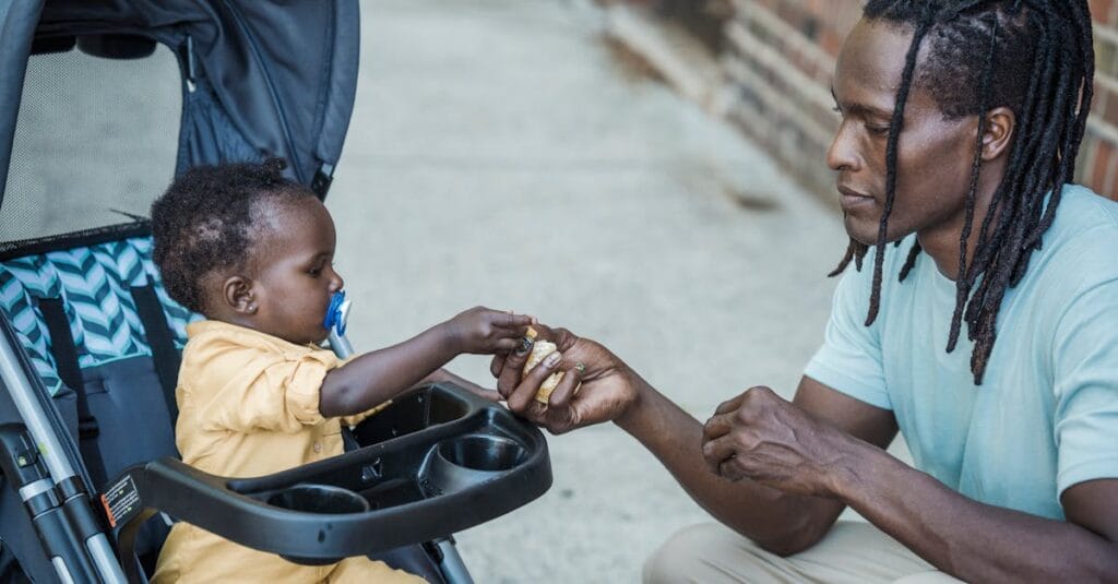 A father and baby bond as they share food outdoors, capturing a moment of love and parenthood.