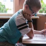 A young boy diligently doing homework at a classroom desk, surrounded by a vibrant learning environment.