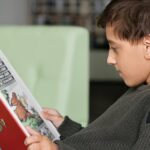 Boy engrossed in reading a book while sitting in a library, creating a tranquil educational atmosphere.