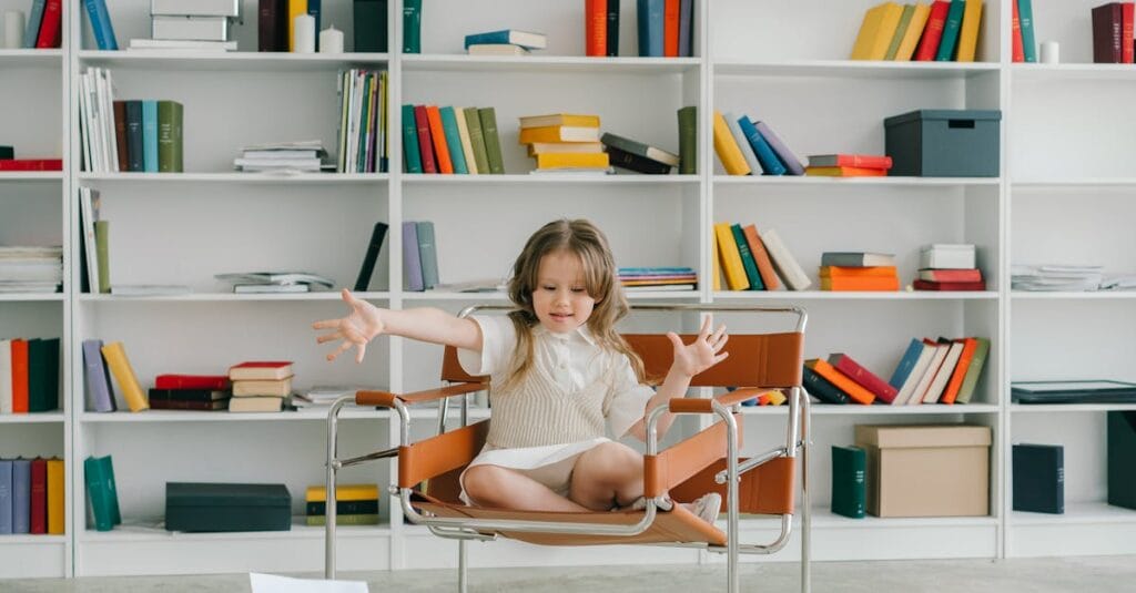 A young girl in a library sitting on a chair surrounded by colorful bookshelves.