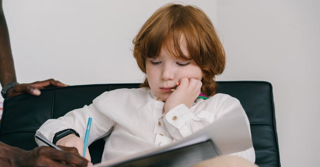 Young boy with freckles focused on drawing during an education session indoors.