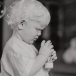 Charming black and white portrait of a toddler with curly hair holding a toy indoors.