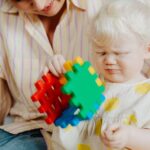 A mother and her albino child enjoy playing with colorful puzzle blocks indoors.