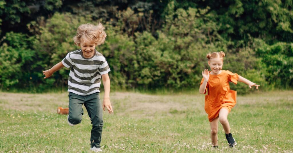 Two happy children joyfully running on a sunny day in a lush green field, enjoying outdoor fun.