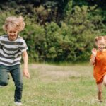Two happy children joyfully running on a sunny day in a lush green field, enjoying outdoor fun.