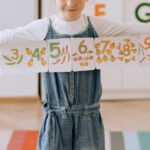 Young girl in a vibrant classroom holding a handmade number banner.
