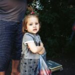 Charming little girl holds a bag of produce at an outdoor market, radiating innocence.