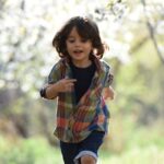 Happy child running in a sunlit orchard during springtime, surrounded by blooming trees.