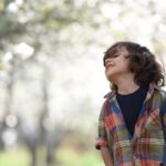 A joyful child in a colorful plaid shirt outdoors, enjoying a spring day.