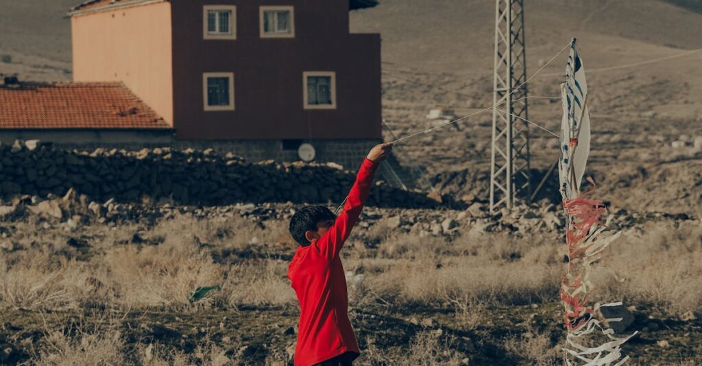 A child plays near a traditional house in İncesu, Türkiye, on a dry grassy field.