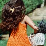 Joyful girl in orange dress runs in yard holding lavender basket, summer scene.