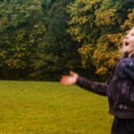 A young girl joyfully plays in a park, throwing autumn leaves in the air.