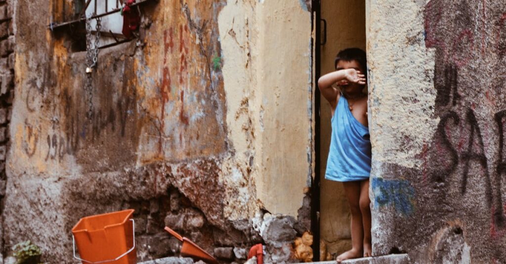 A young child peeks out from a worn building entrance in a vibrant urban street.