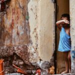 A young child peeks out from a worn building entrance in a vibrant urban street.