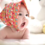 Charming baby with colorful scarf surrounded by cute plush toys, highlighting innocence indoors.