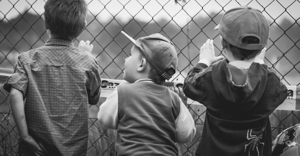 Black and white image of three young boys peering through a chain-link fence.