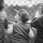 Black and white image of three young boys peering through a chain-link fence.
