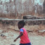 A joyful child in a colorful outfit running and playing with a bicycle tire outdoors.