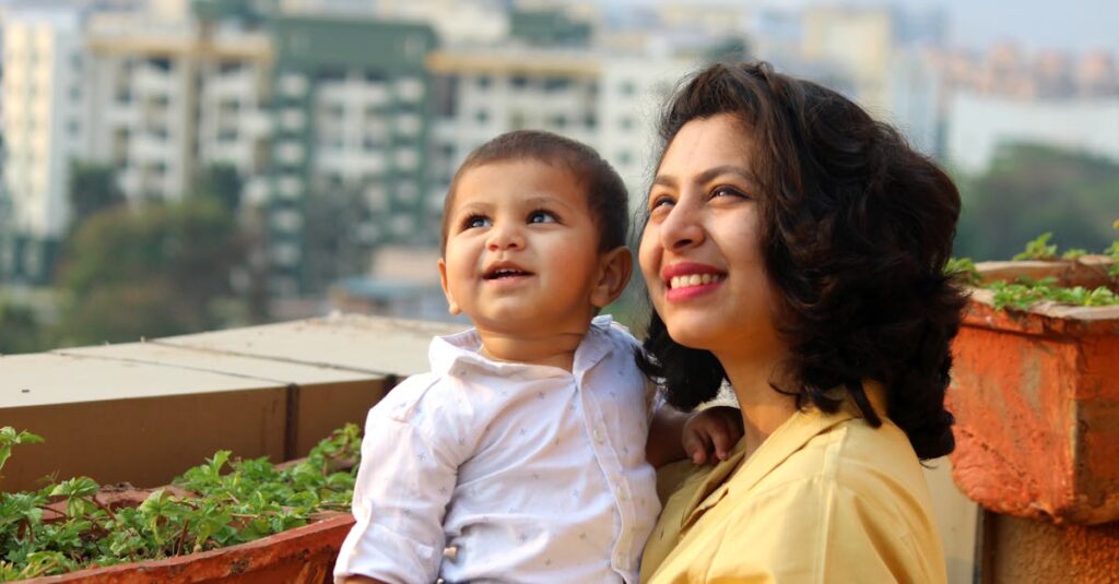 Mother and baby enjoying a sunny day on a balcony with a cityscape backdrop.