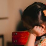 A young girl engrossed in reading a book in an indoor classroom setting.