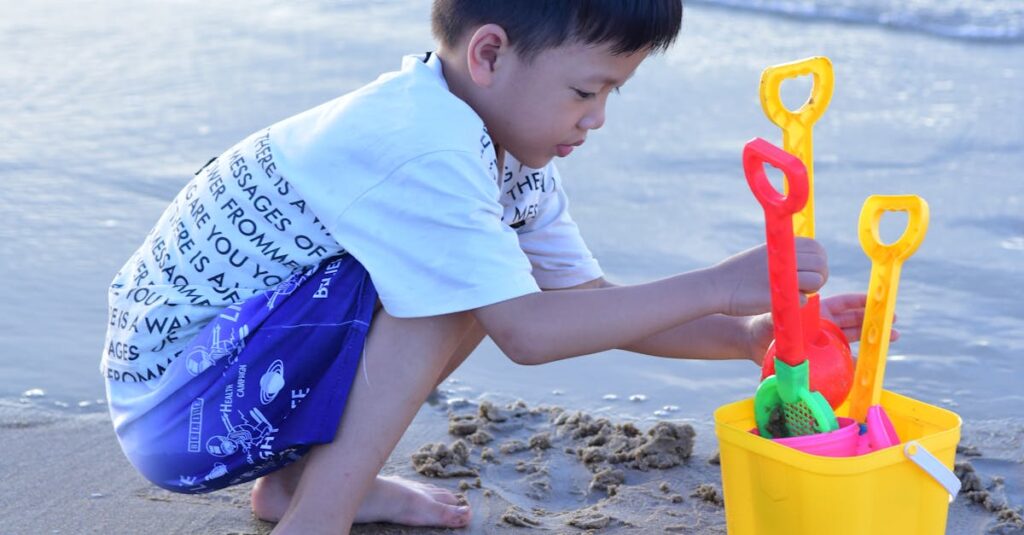 Young boy enjoys building sandcastles with colorful toys by the ocean shore on a sunny day.