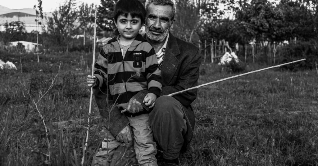Black and white portrait of a grandfather and grandson bonding in nature, holding sticks.