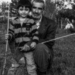 Black and white portrait of a grandfather and grandson bonding in nature, holding sticks.