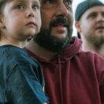 A father and his child enjoying a live outdoor music concert in daylight.