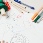 A child engages in creative drawing with colored pencils surrounded by wooden toys on a table.