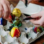Children decorating colorful Easter eggs on a wooden table, engaging in a fun and creative activity.