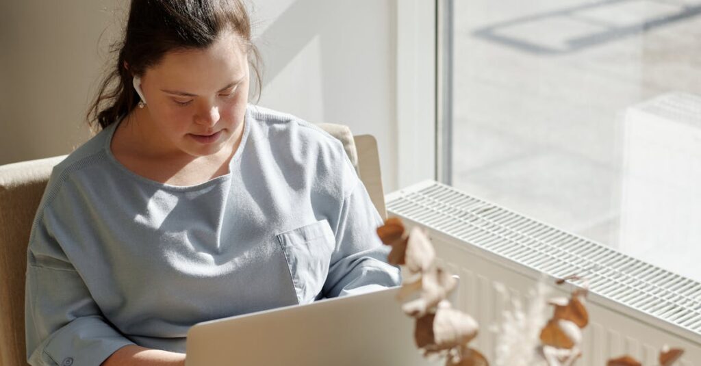 Young woman with Down syndrome working on a laptop by a sunlit window in a cozy cafe.