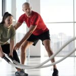Woman and trainer engaging in rope workout in a bright gym, showcasing inclusivity and fitness motivation.