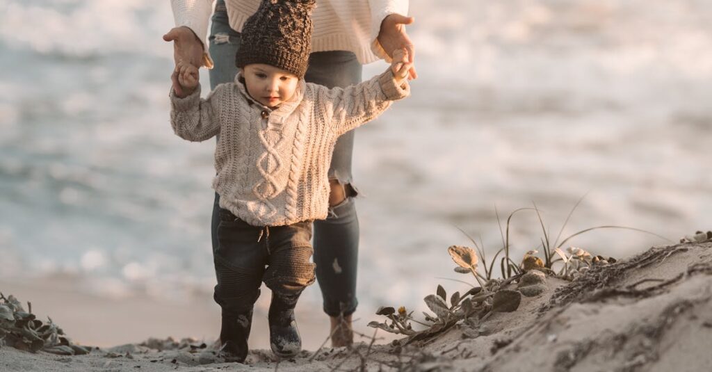 A mother and toddler walk hand in hand on a sandy beach during a serene day.