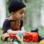 A young boy in casual attire plays with colorful toys on a lawn, enjoying an outdoor moment.