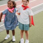 Two young girls wearing capes share a joyful moment on a school playground.