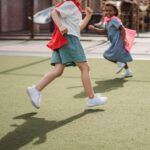 Two children happily running with capes, enjoying playtime on a sunny day outdoors.