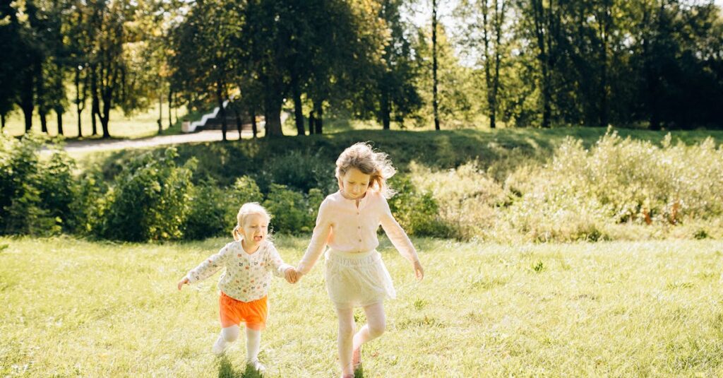 Two young girls holding hands and running on a grassy field in a sunny park setting.