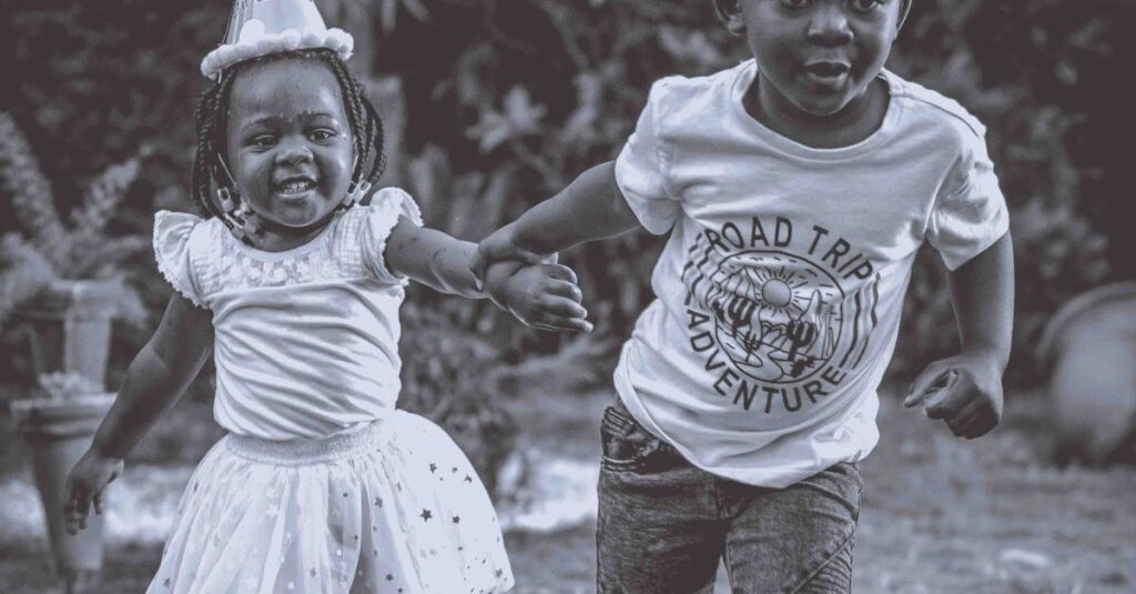 Two children happily running outdoors wearing birthday hats, enjoying a fun celebration.