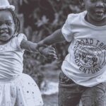 Two children happily running outdoors wearing birthday hats, enjoying a fun celebration.