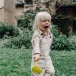 Cute little boy with plastic rake on lawn with fresh green grass in yard