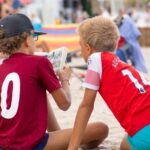 Two kids enjoying a book on Kolobrzeg beach, capturing a moment of summer relaxation.