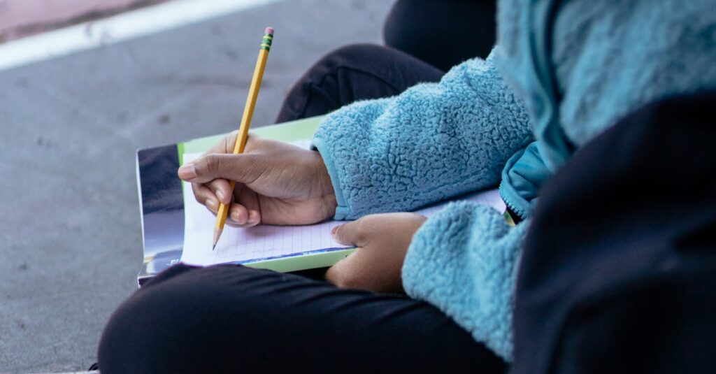 A young girl writing with a pencil while sitting outdoors in casual attire.