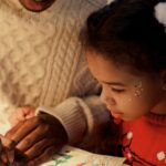 Father and daughter enjoying quality time crafting a Christmas letter with colorful materials.