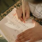 A child drawing on paper with colored pencils, composing a Christmas wish list.