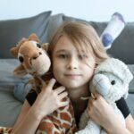 A young girl enjoys her time indoors, cuddled with stuffed toys on a cozy bed.