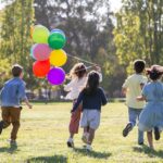 Children happily running with balloons in a sunny park, capturing friendship and joy.