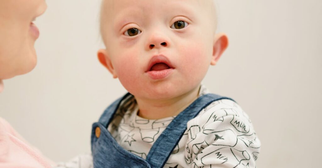 Adorable baby with Down syndrome in blue overalls, held by an adult indoors.