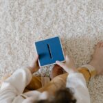 A child sits on a soft carpet holding a blue piggy bank, top view.