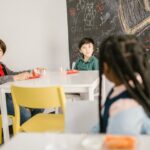 Children sitting in a classroom with snacks and a chalkboard background.