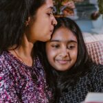 A loving mother and daughter share a bonding moment while reading a book indoors.